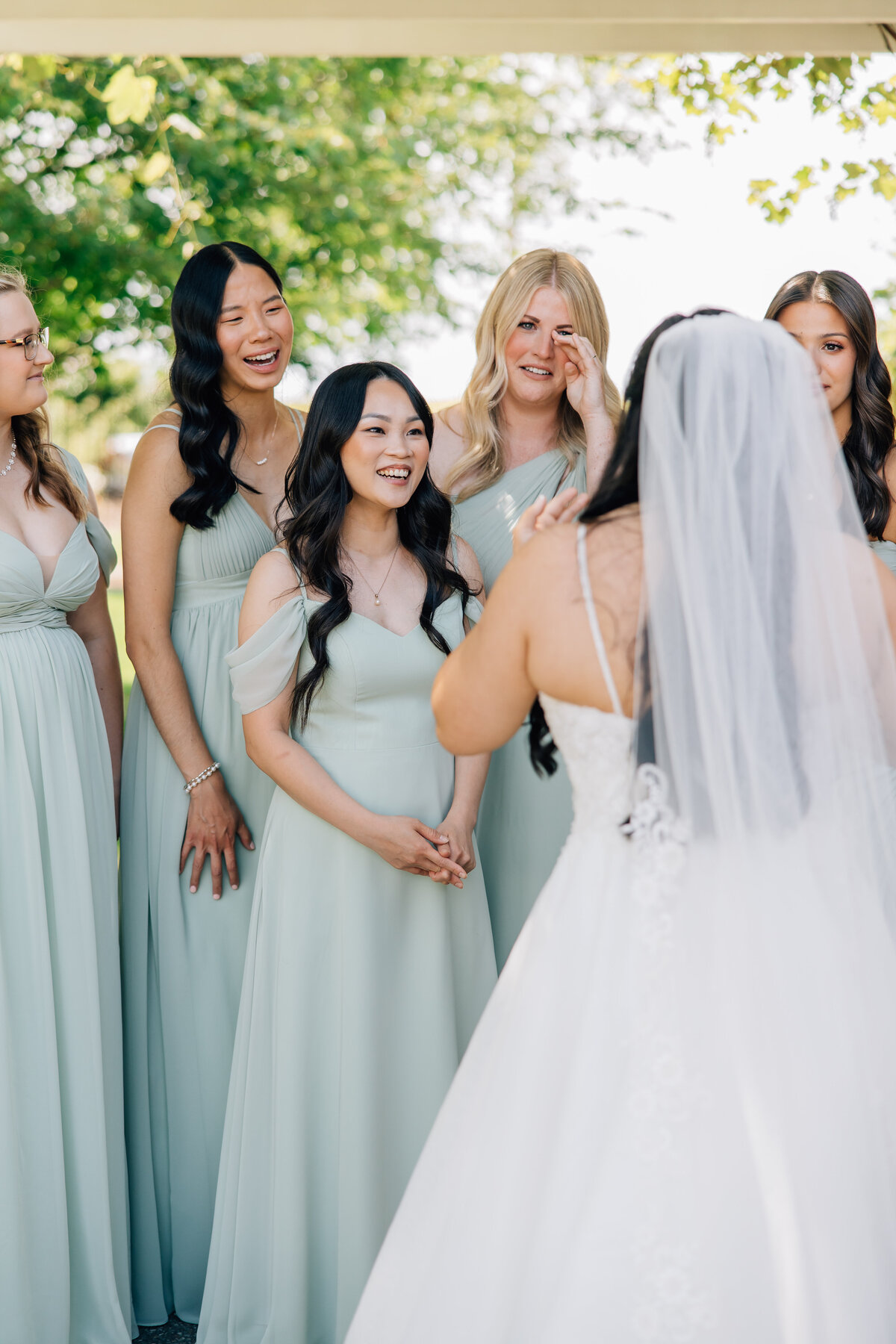 Bridesmaids in sage green dresses tearing up as they see the bride for the first time during a bridesmaid first look