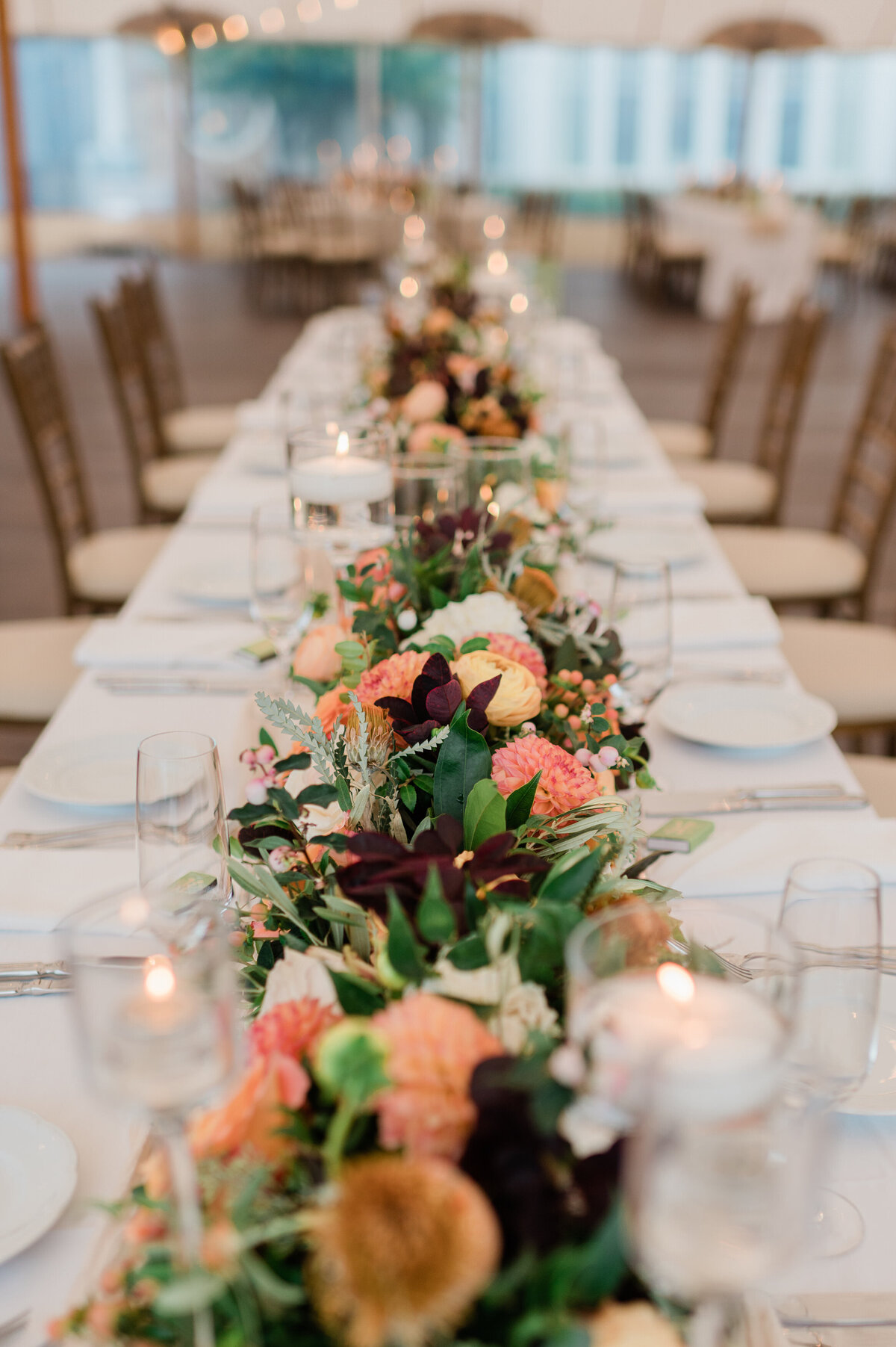 A close-up of the reception’s head table, with a floral garland and flickering candles in glass holders.