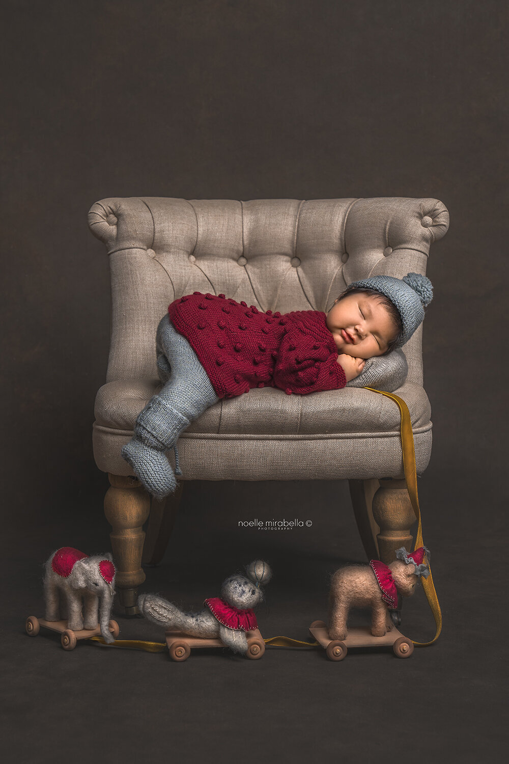 Baby sleeping on linen chair with vintage circus pull toy.