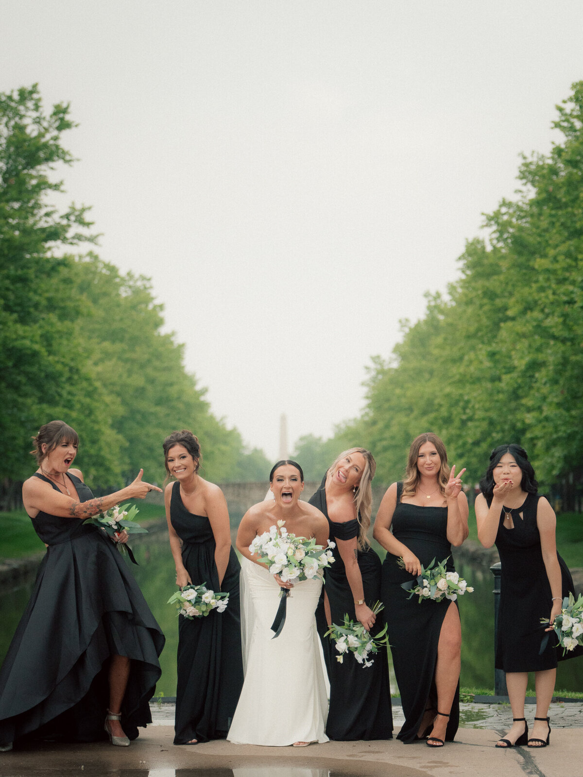 Bride with bridesmaids in black dresses by canal