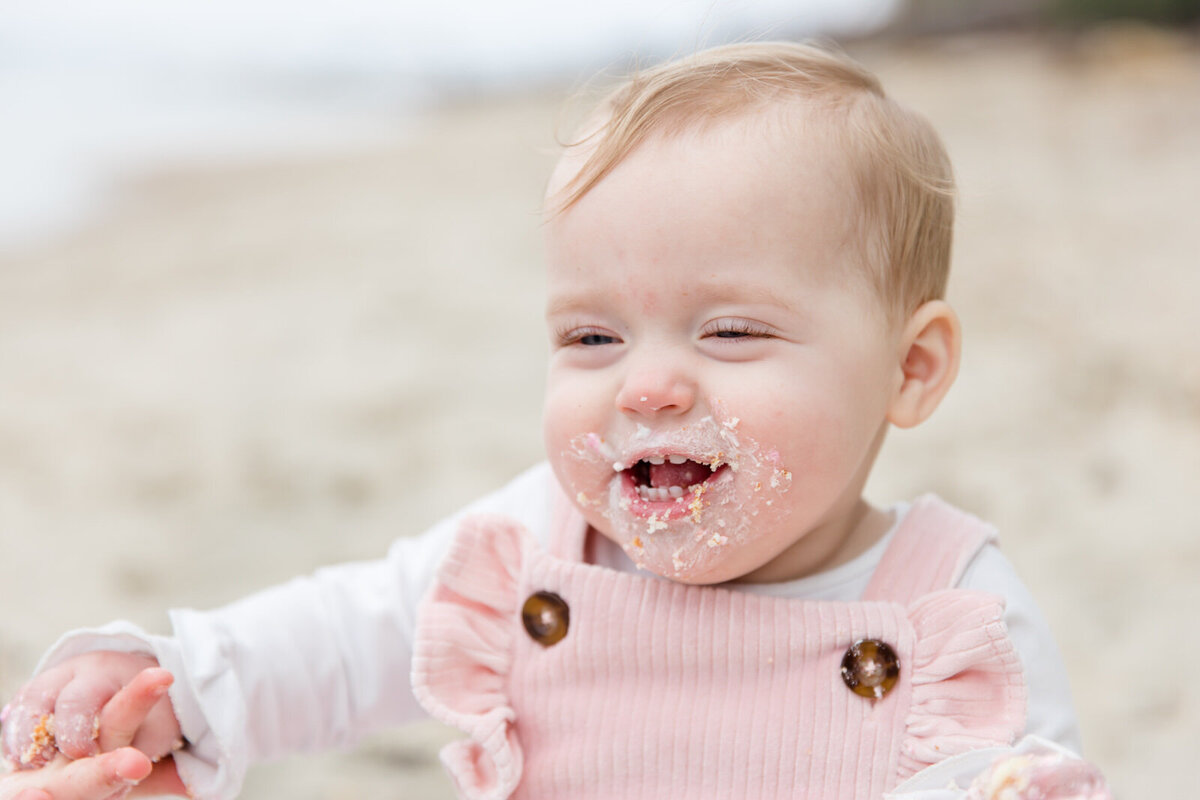 Birthday girl smiles with cake frosting all over face during cake smash photo session