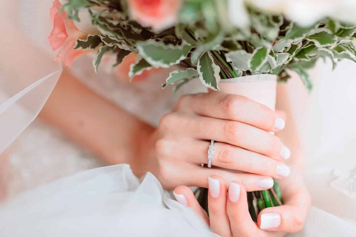 Close up of brides hands holding a bouquet of greenery and florals