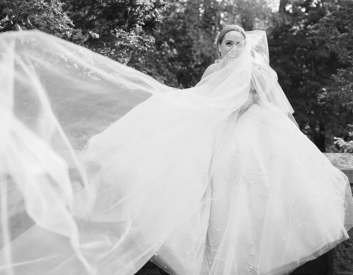 Joyful bride with her veil caught in the wind in black and white