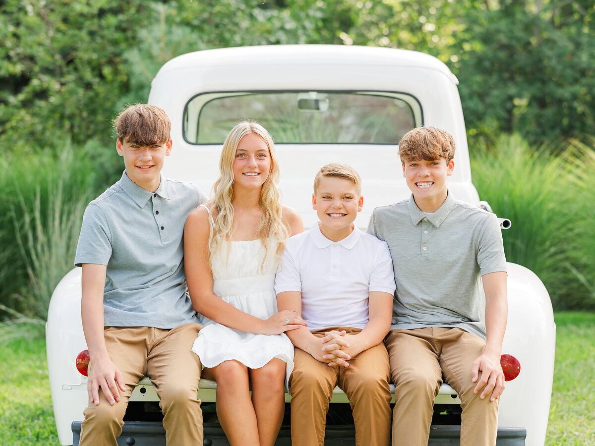 Brothers and a sister sitting in the back of a truck outdoors for Erie County family photography.