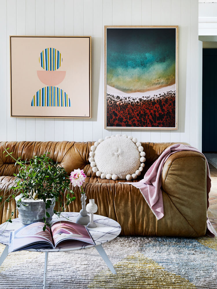 Colourful modern art above leather sofa in relaxed Melbourne living room with round coffee table and greenery.