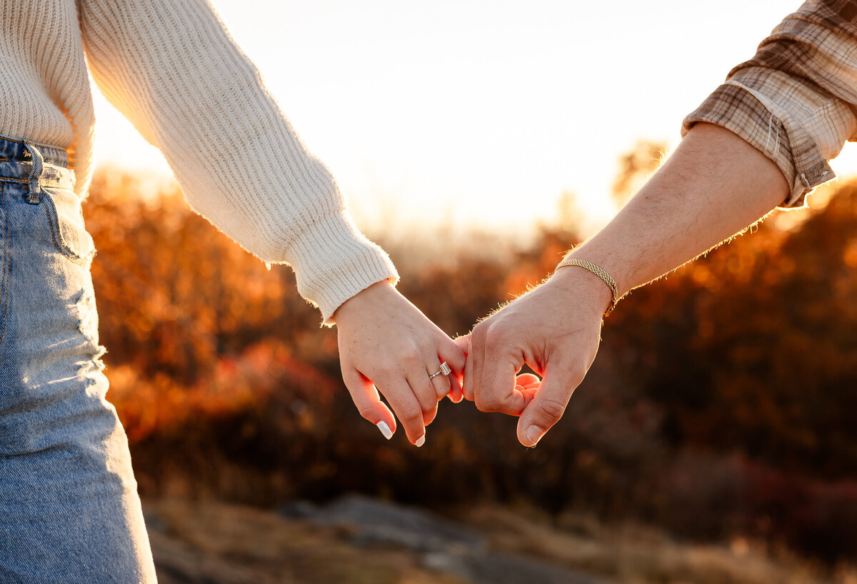 couple holding pinky finders at with engagement ring glowing in the sun