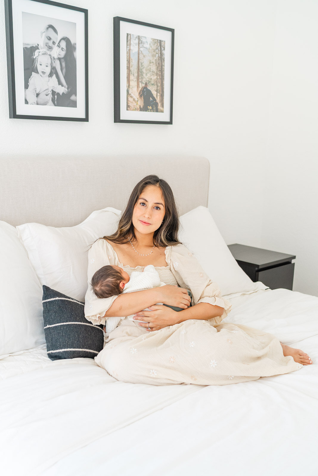 a mother sits on her bed with her sleeping newborn in her arms during her newborn session in Round Rock.