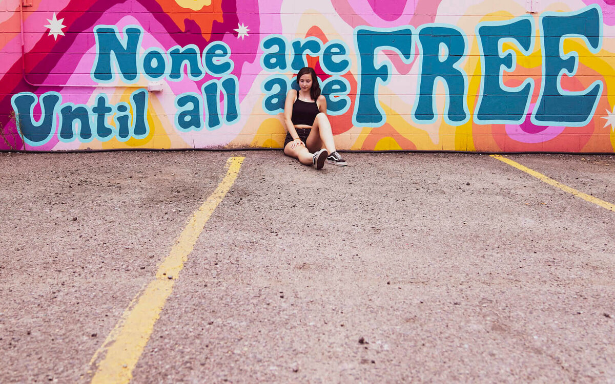 denver photographers senior pictures - girl sitting against wall with artwork