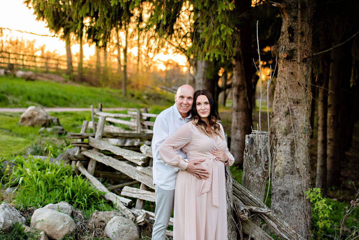 husband and wife standing next to a wood fence for their Toronto farm maternity photos