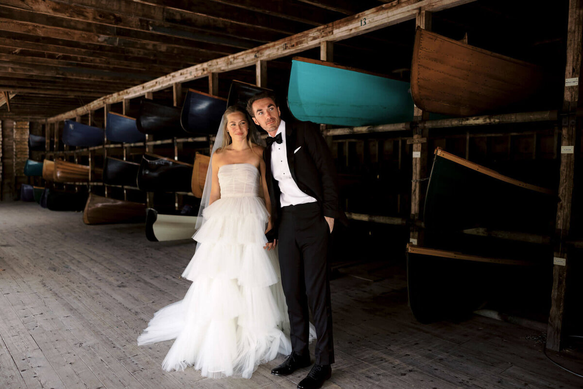 The bride and the groom are inside a room where there are many canoes stored at The Ausable Club, New York.