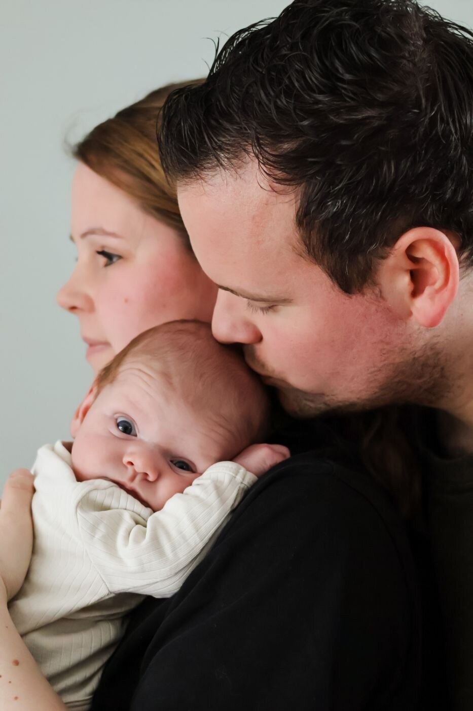 Het vredige gezicht van een pasgeboren baby, met de ouders op de achtergrond, wat hun nabijheid en liefde benadrukt