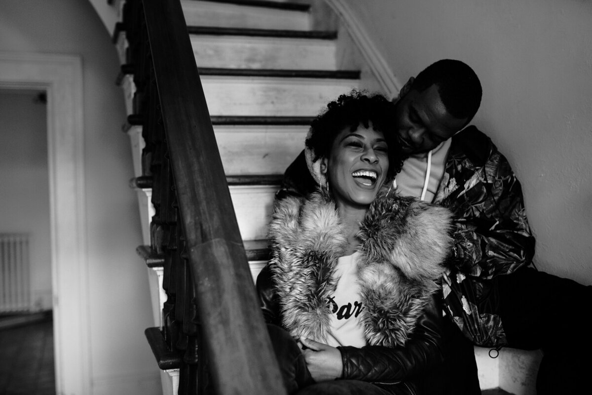 Couple laughs on the stairs of their home during their engagement session