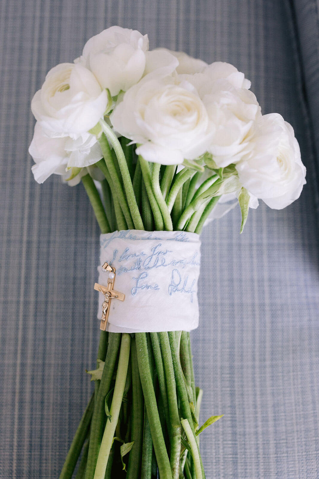 A bouquet of white flowers is tied with an embroidered white cloth with a crucifix attached, in Wianno Club, Cape Cod, MA.