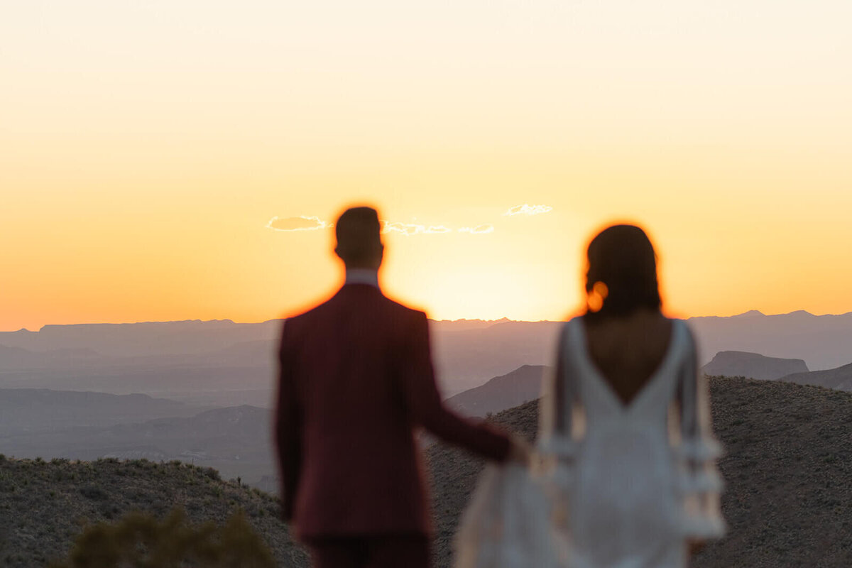 couple walking into sunset with desert and mountains in front of them