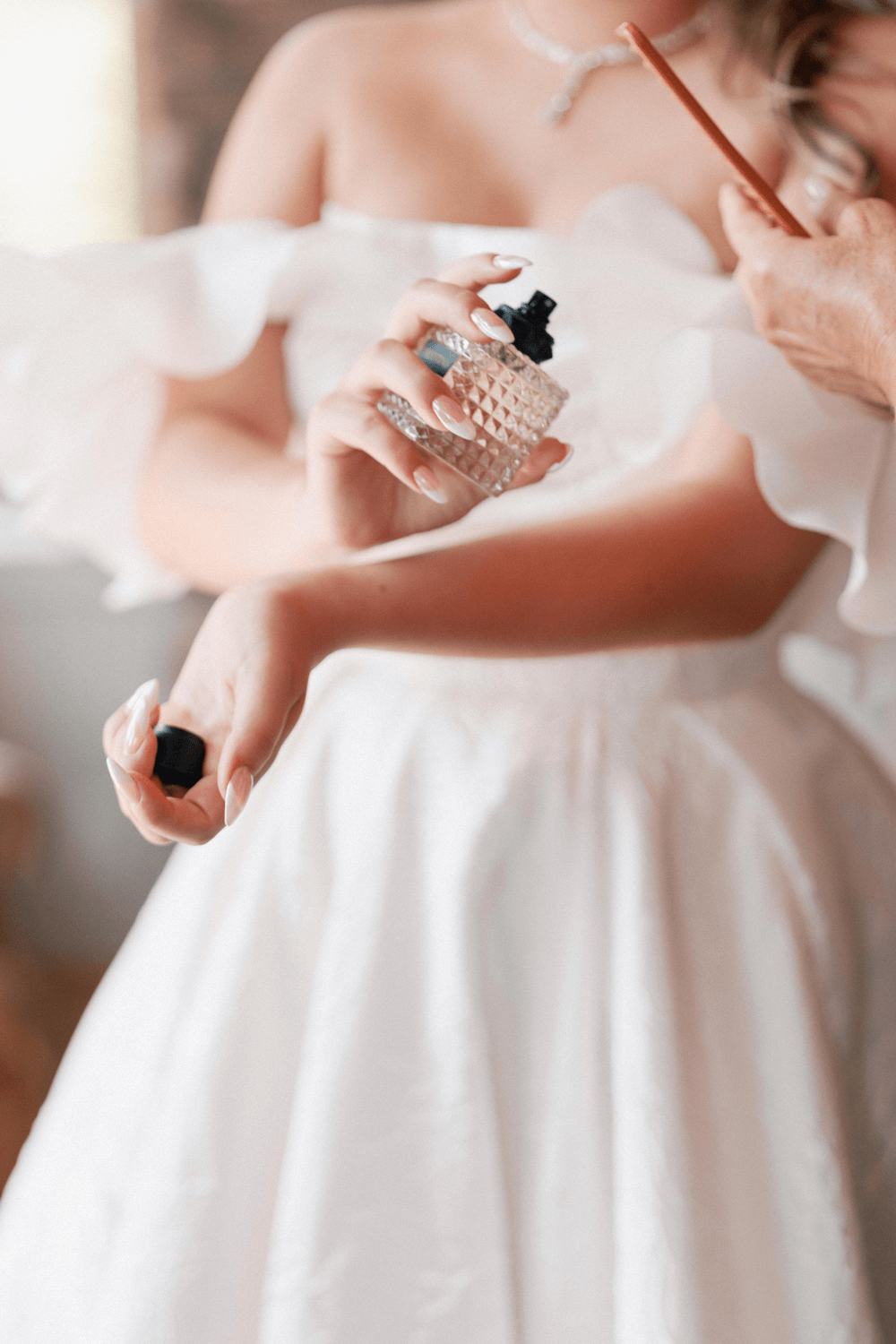 Bride applying perfume before her pastel wedding at Moonlight Basin, wearing a floral-textured gown with soft off-the-shoulder sleeves.