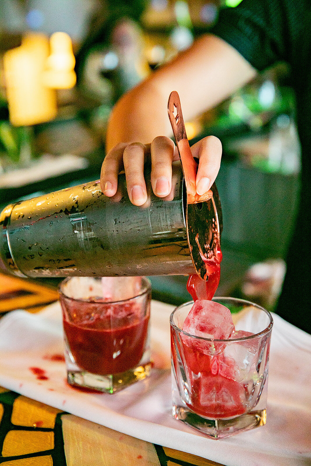 Bartender pours a red cocktail into ice-filled glasses during an evening event.