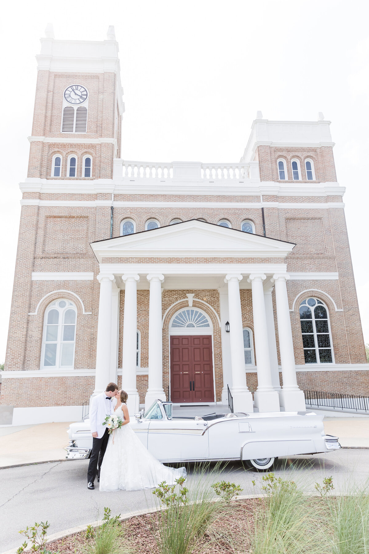 bride and groom on wedding day with antique car at the our lady of the gulf catholic church