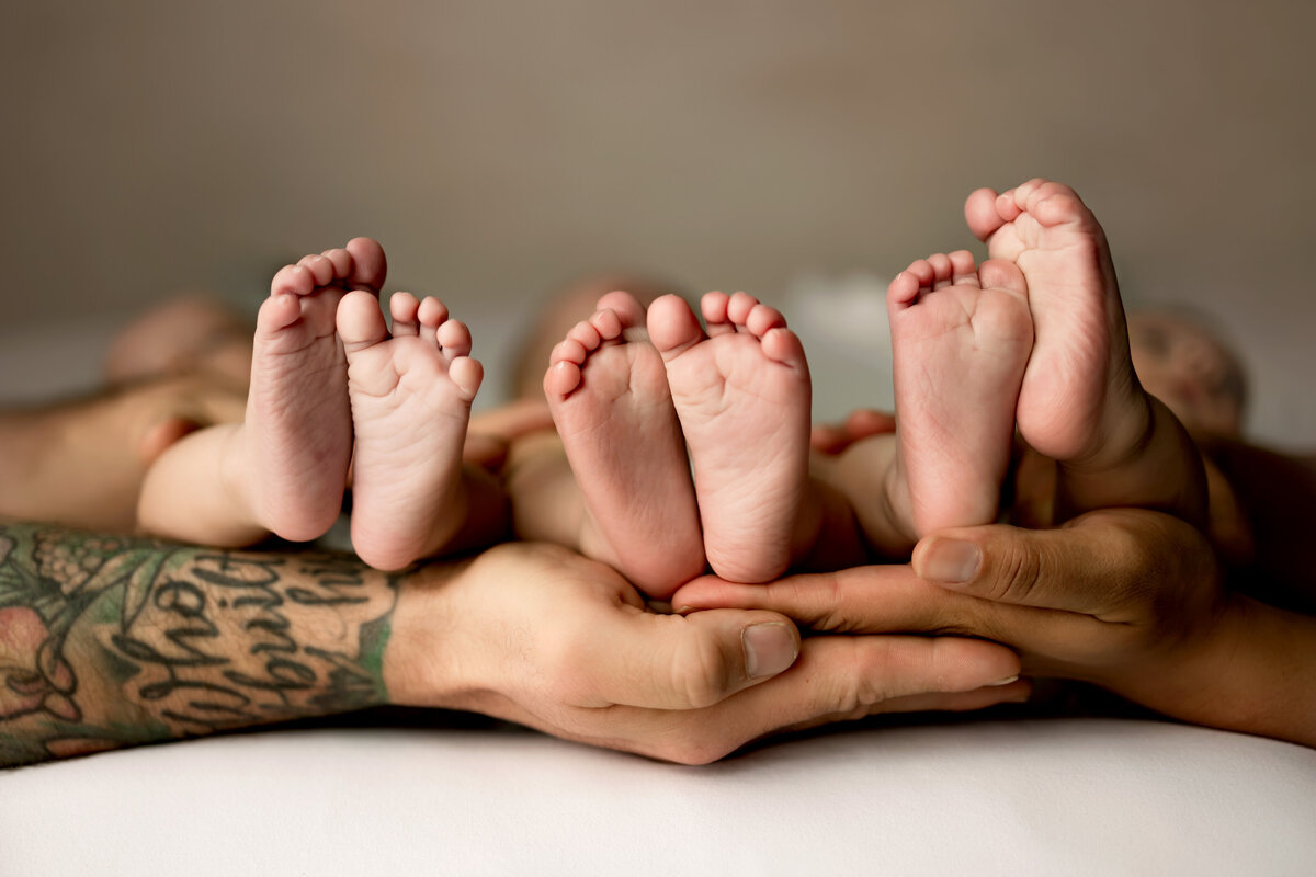 Newborn triplets feet held in parents hands for newborn pictures in Denver