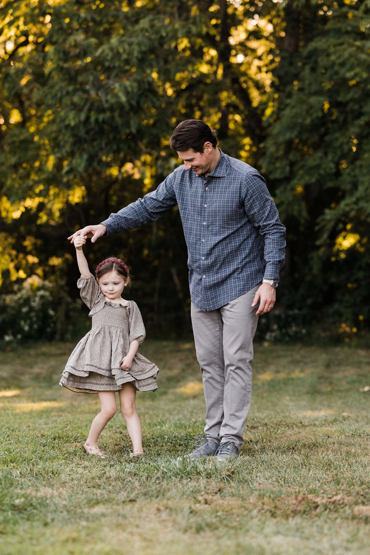A Pittsburgh family photographer captures a touching moment of a man assisting a young girl in a twirling dance move on a grassy field.