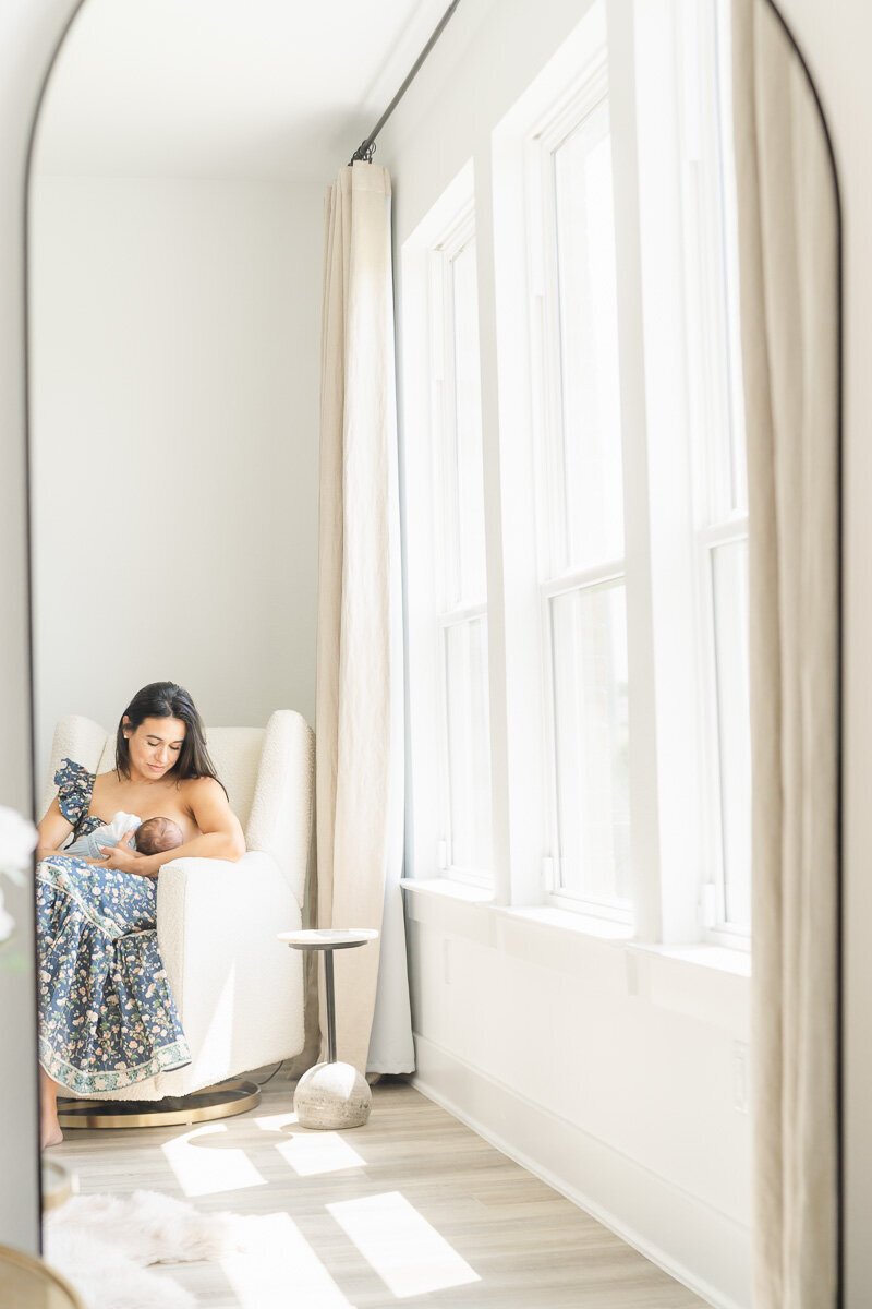 a mother sits on a rocking chair while nursing her newborn and is captured through a mirror by a Leander newborn photographer.