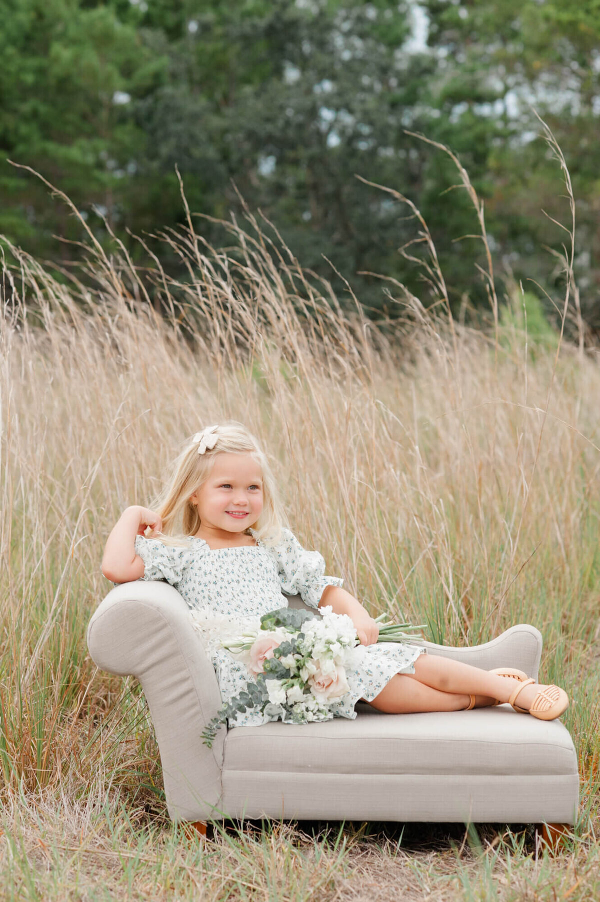 Young daughter sitting on beautiful neutral couch and smiling at her daddy while holding a flower bouquet