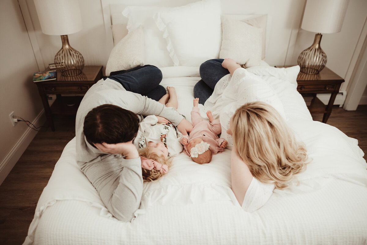 A candid moment between a family of four cuddling together on the bed facing one another.
