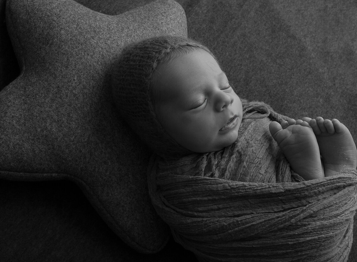 Black and white newborn image. Baby is swaddled and laying atop of a large felt star pillow. Captured by top Brooklyn newborn photographer Chaya Bornstein