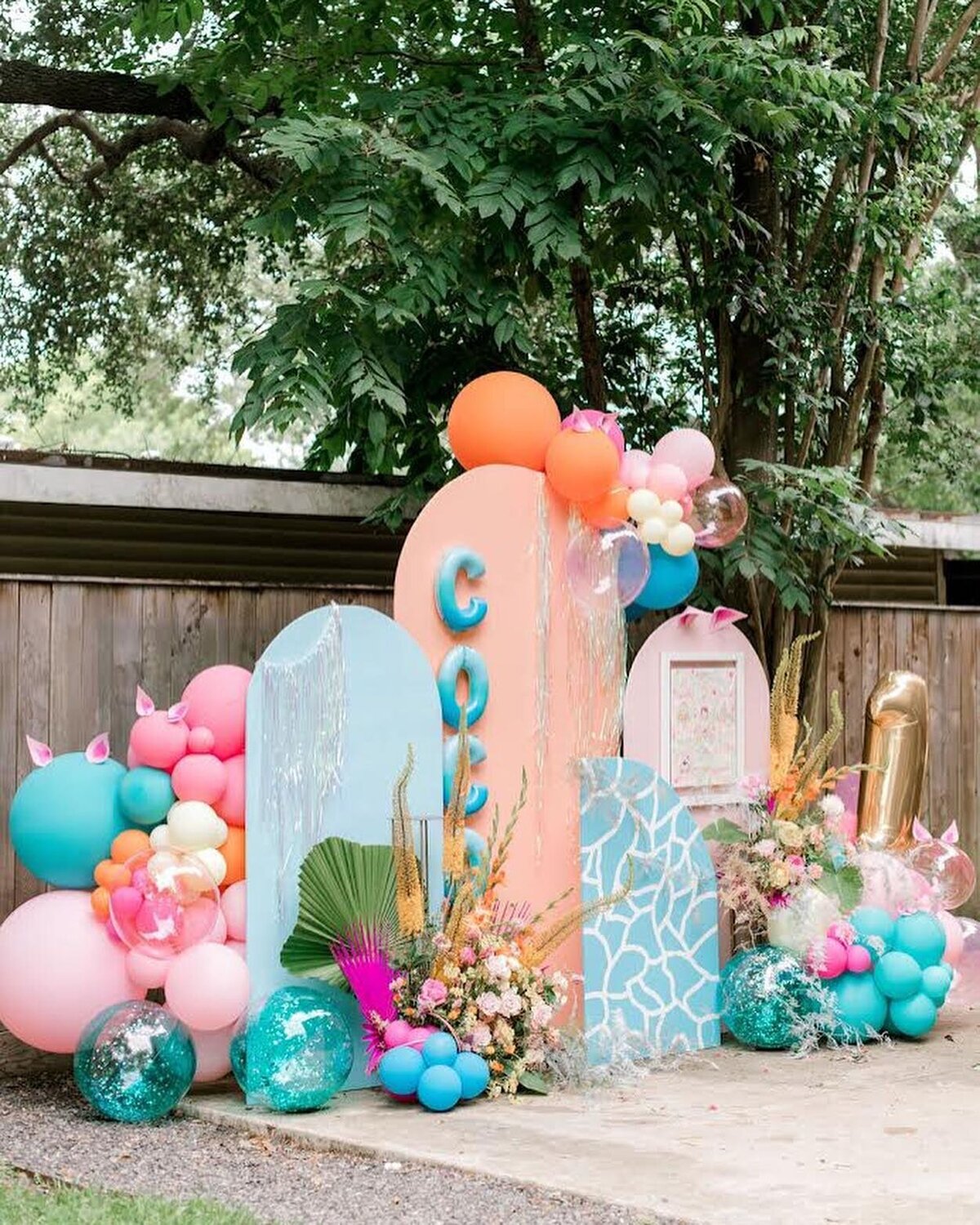 Pink, orange and blue colored arch party backdrop decorated with balloons and florals