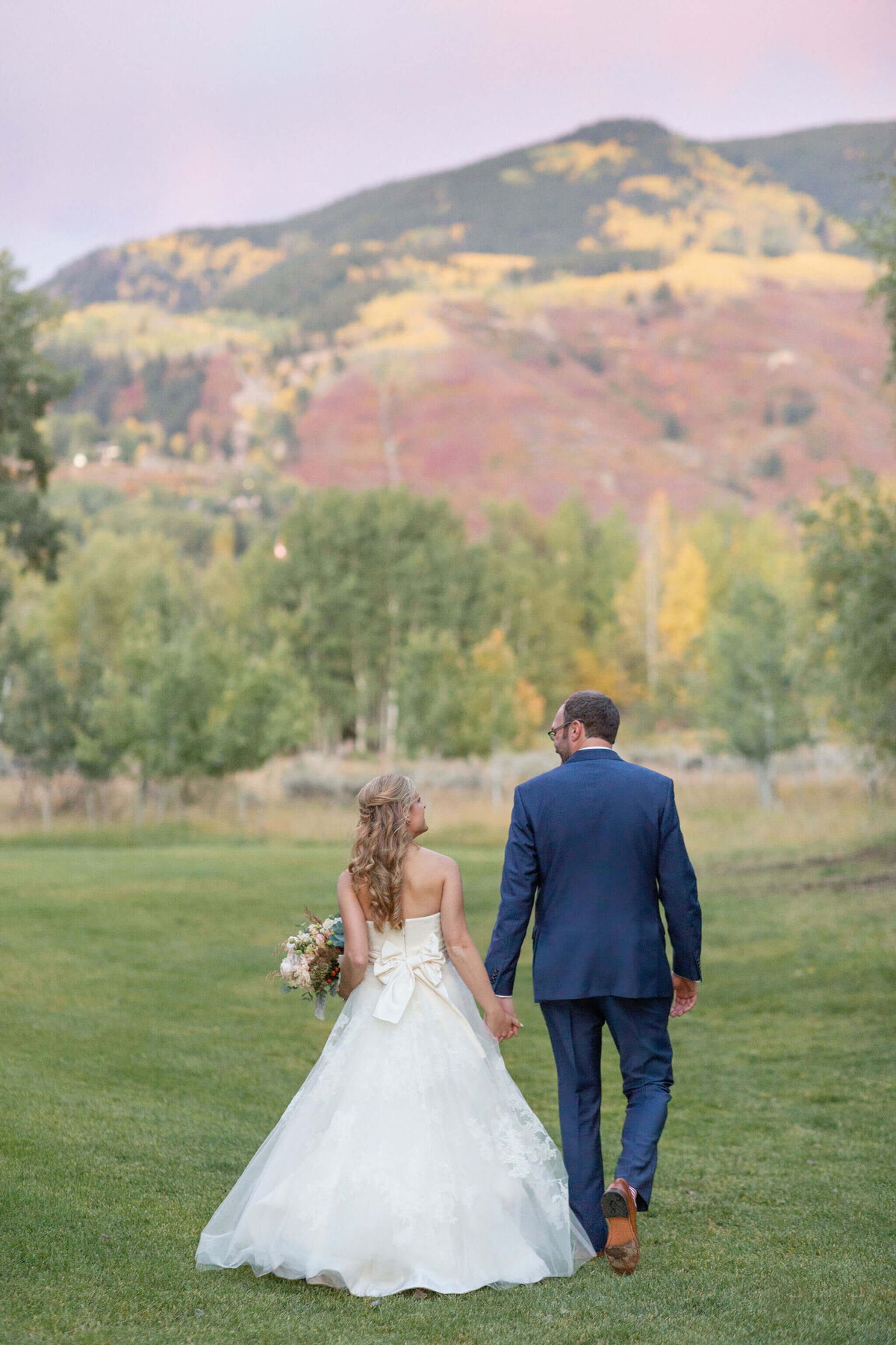 bride and groom seen from behind walk with yellow aspen trees in background