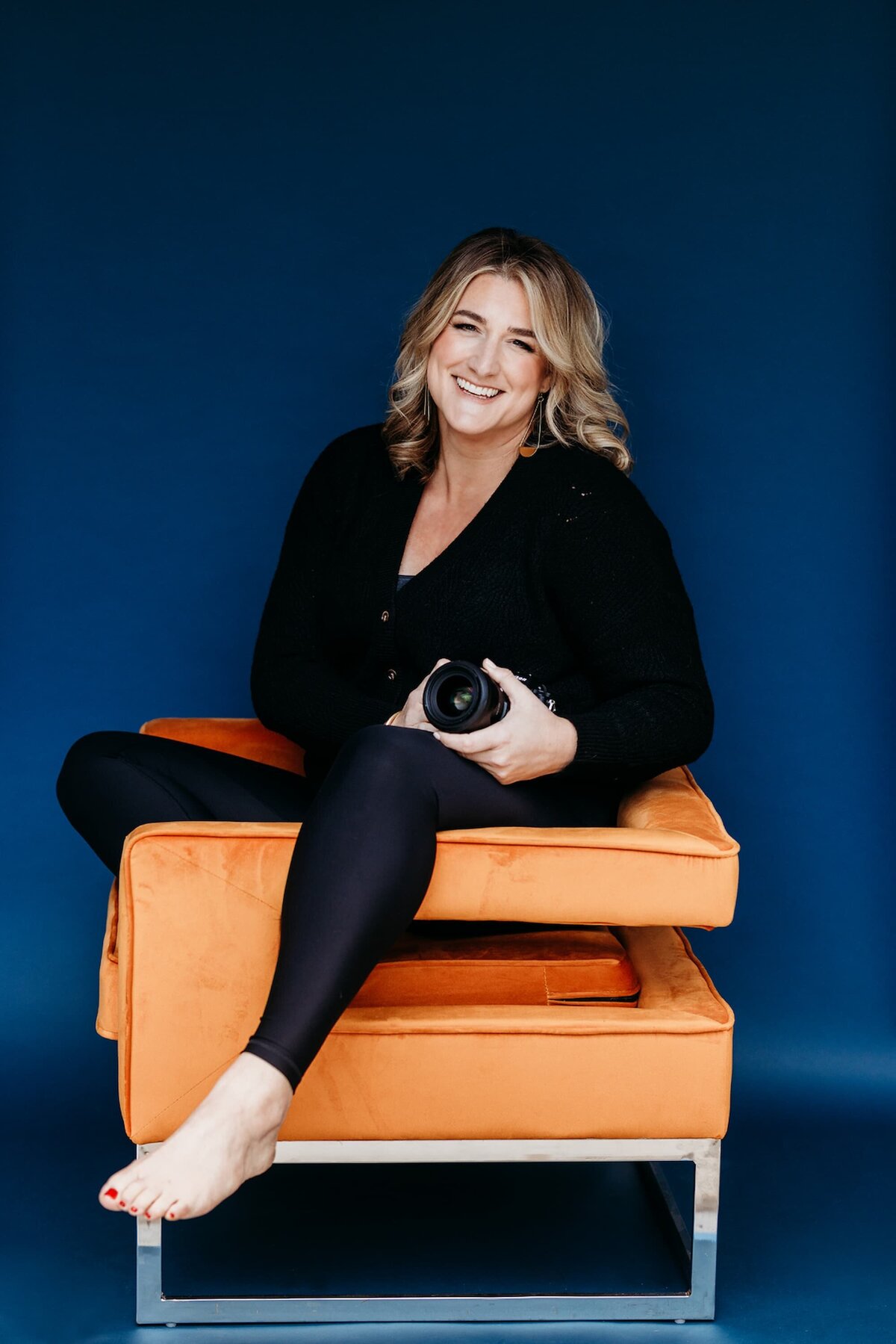 Jen Rizy, Austin maternity photographer, smiling while seated in studio with camera
