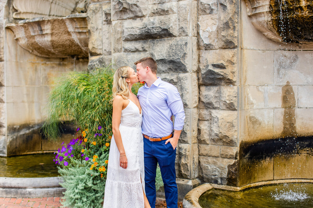 engaged couple kissing by water feature