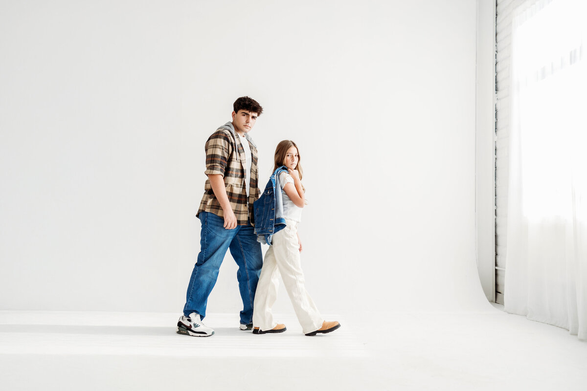 Brother and Sister walk towards window while looking at the camera in a Denver photo studio