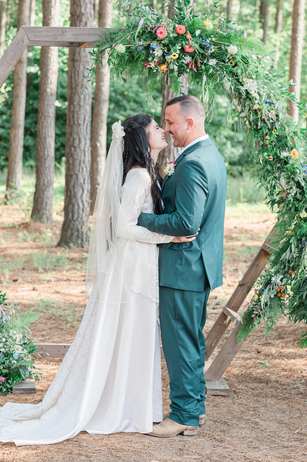A wedding couple standing in front of a geometric arch about to kiss