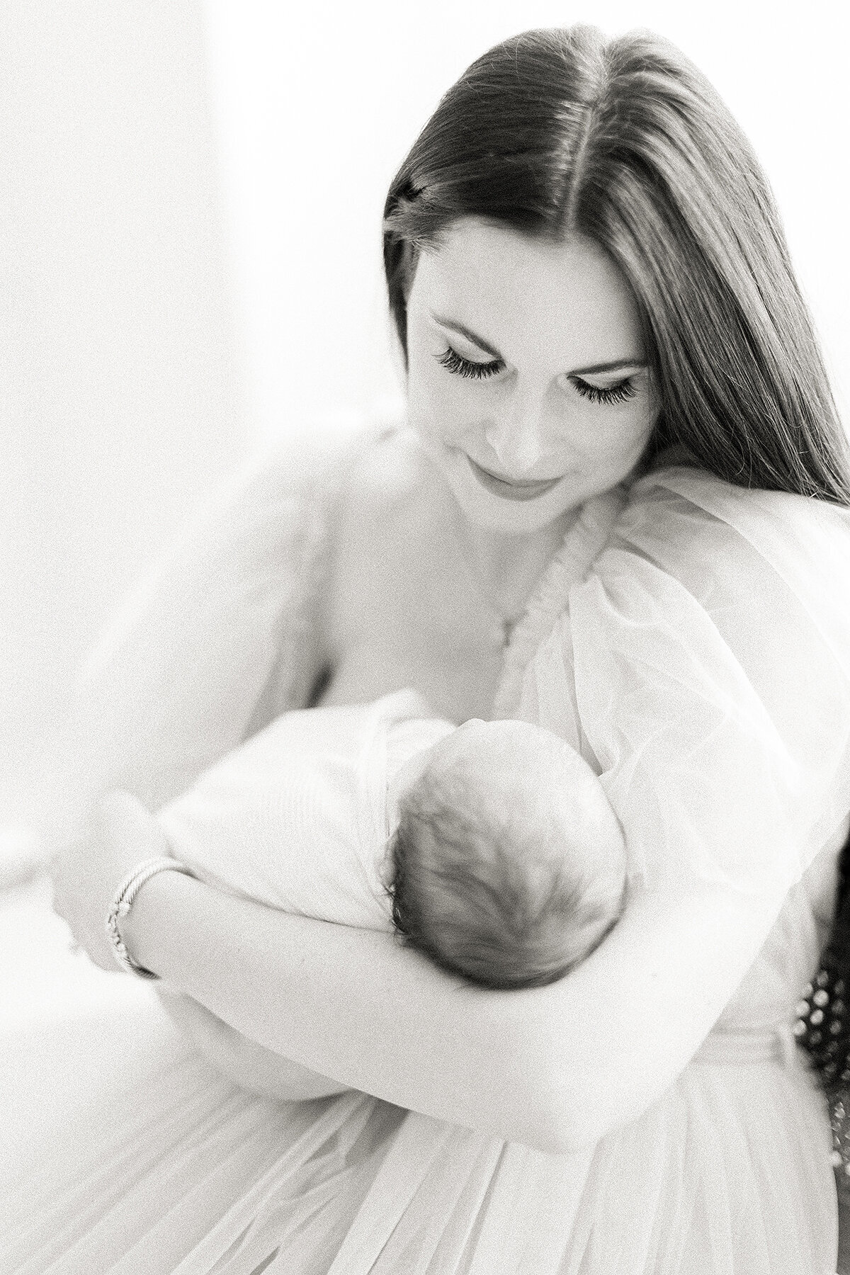 Close up black and white photo of a mother dressed in a tulle gown while she holds her newborn baby boy and looks down at him.
