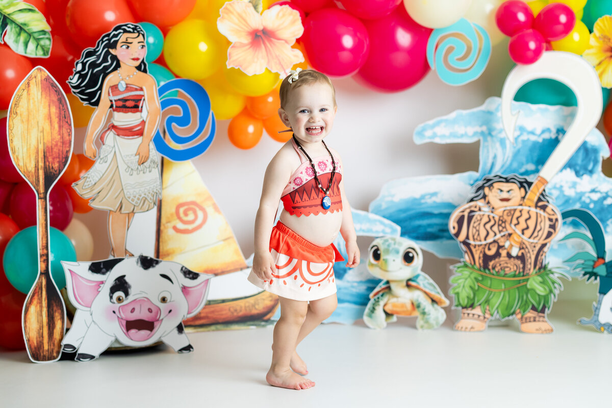 Girl having fun dressed in Moana costume surrounded by photo props for a festive birthday photoshoot.