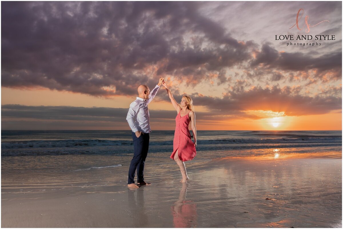 Wide angle shot of engaged couple dancing on Siesta Key Beach with the sun setting behind them