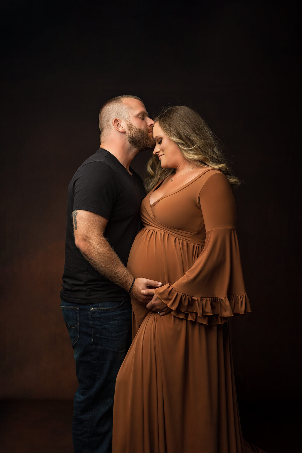 A husband kisses the forehead of his expectant wife during their luxury maternity session in Minnesota.