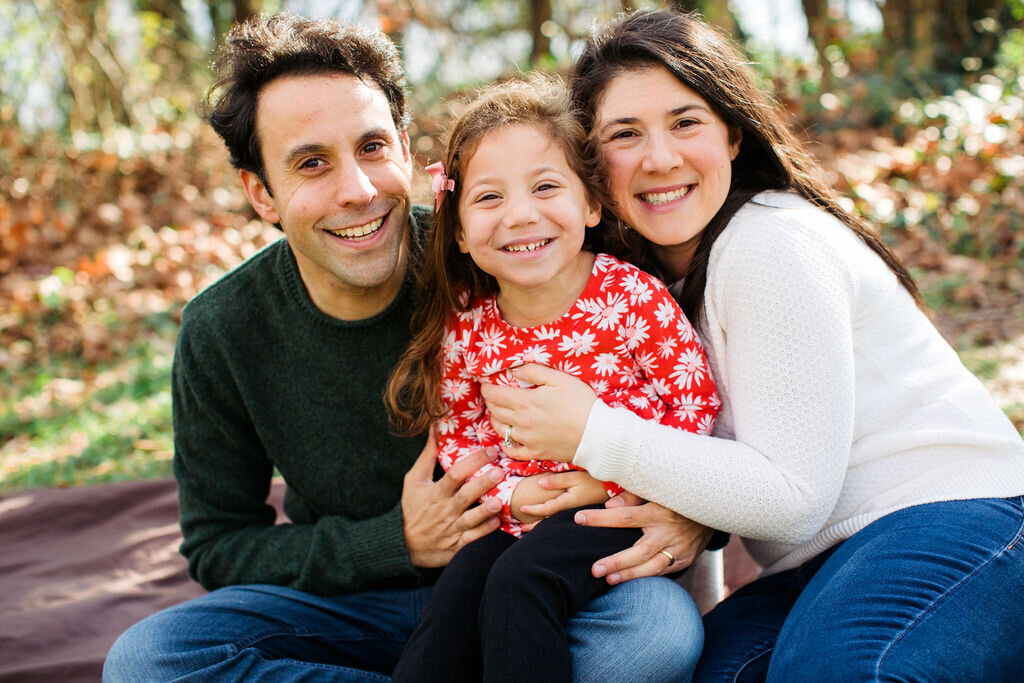 A family of three hugs each other closely in fall.