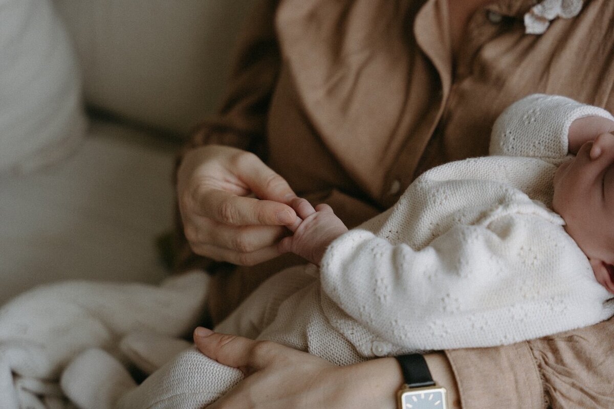 Gros plan sur les mains de la mère tenant celles de son bébé endormi. Séance naissance intime par Kamescop, photographe maternité en Bretagne.