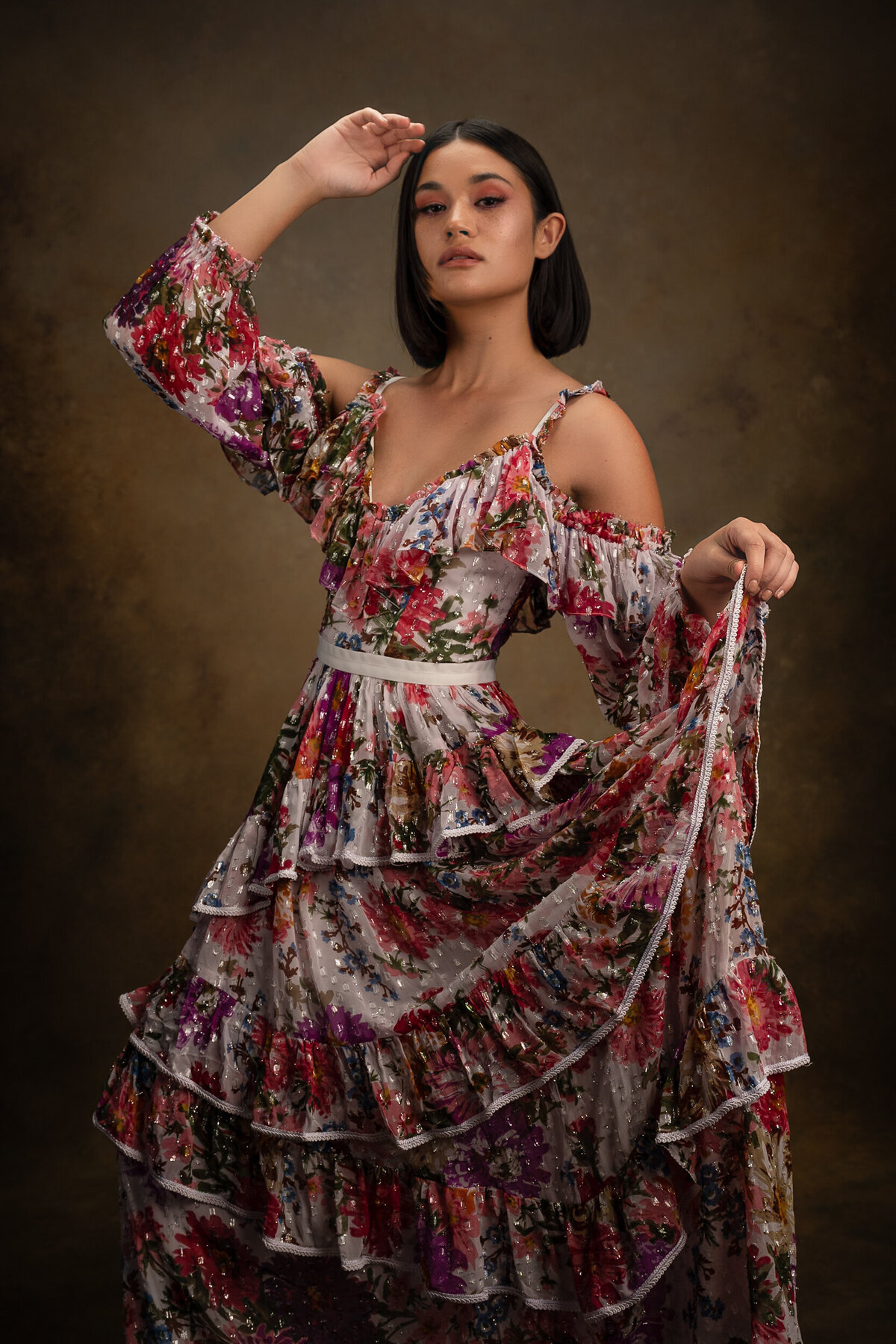 Young woman with dark short hair wearing a flower gown touching her hair and looking down to the camera