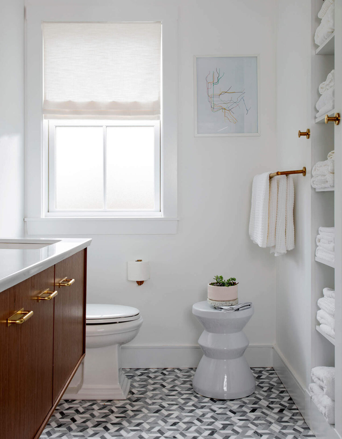 Milton new construction home interior designer designs a kid-friendly bathroom with a natural wood vanity, stone mosaic flooring, simple white walls, and brass fixtures.