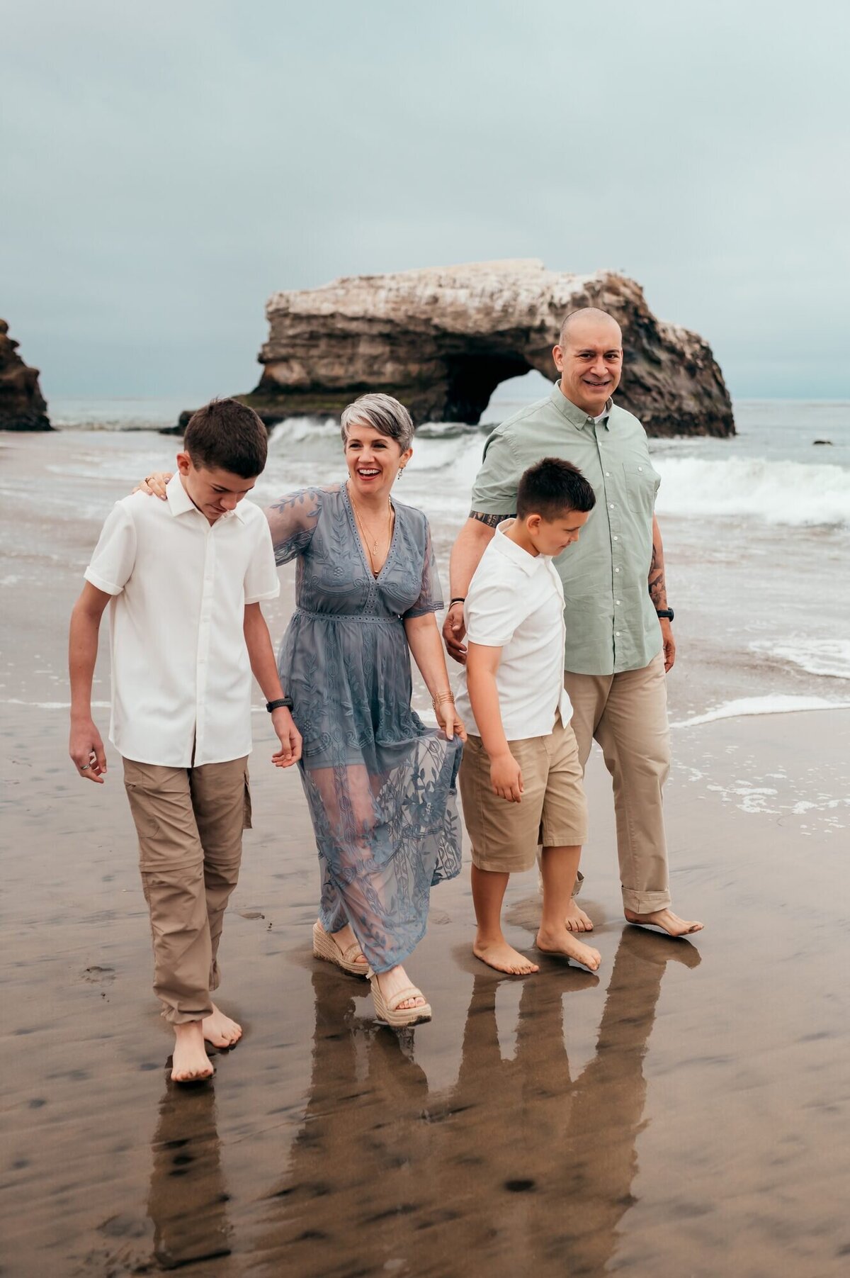 Family of four walking along the wet sand with the Natural Bridges arch behind them in Santa Cruz