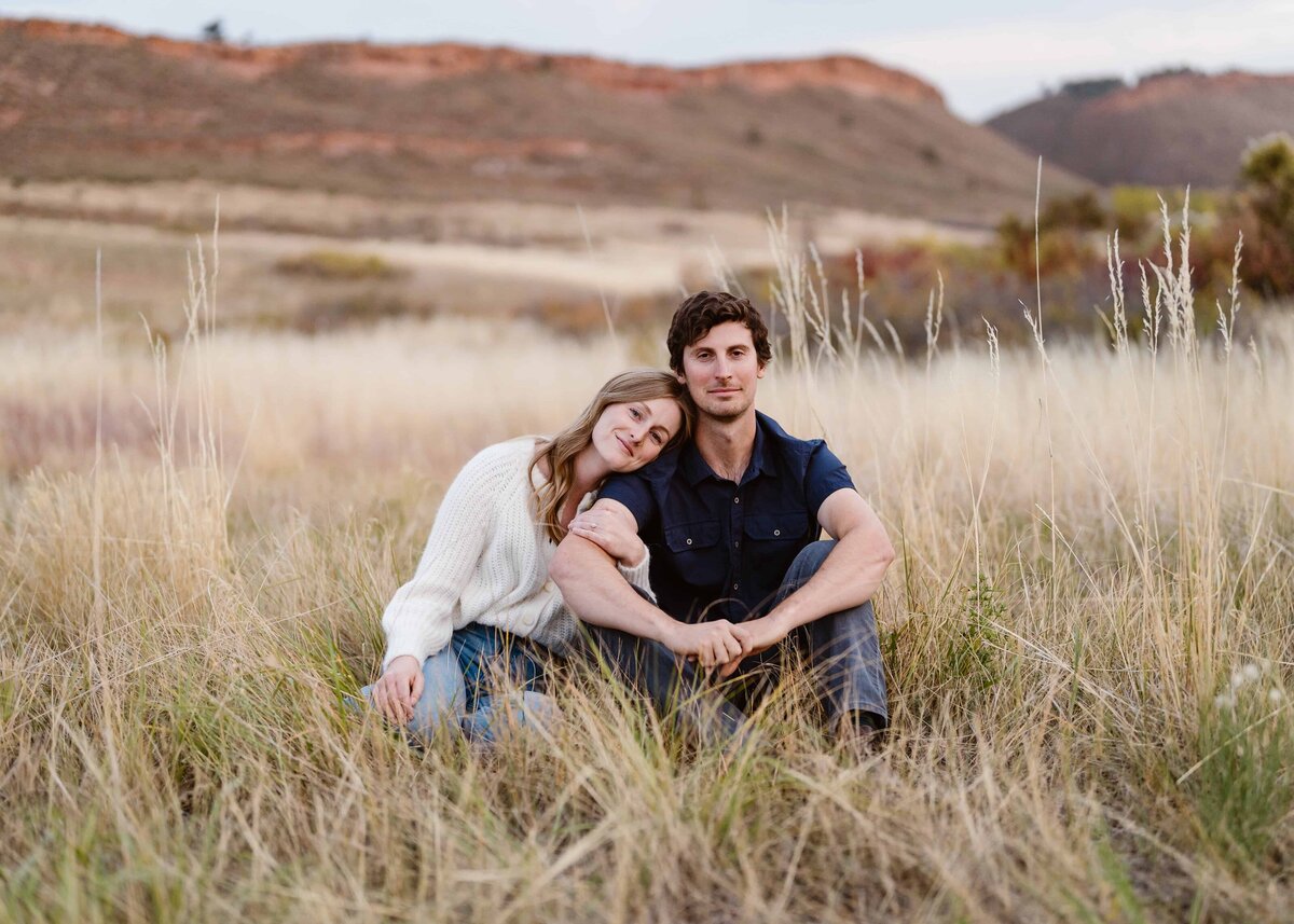 Couple sitting close together in a grassy Fort Collins, Colorado meadow during golden hour, captured by a Colorado Wedding and Portrait Photographer.
