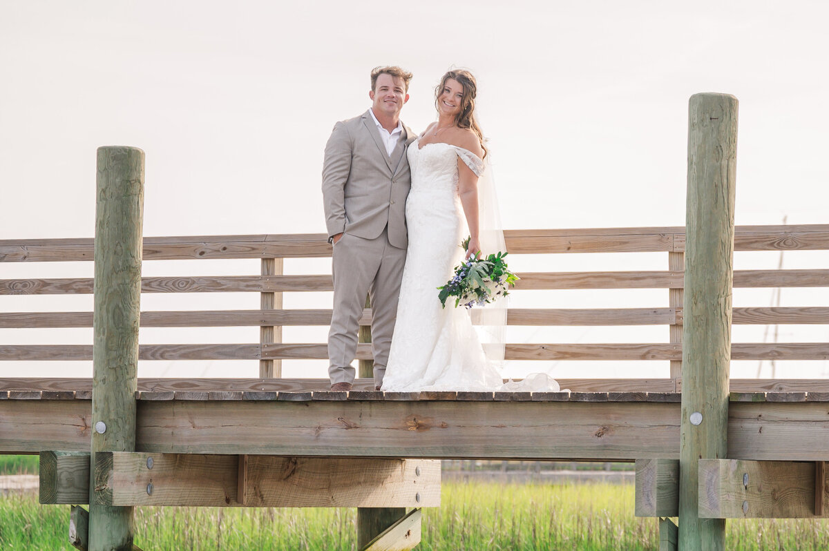 A married couple smiling on a bridge overlooking the intracoastal waterways in South Carolina by JoLynn Photography, a destination wedding photographer