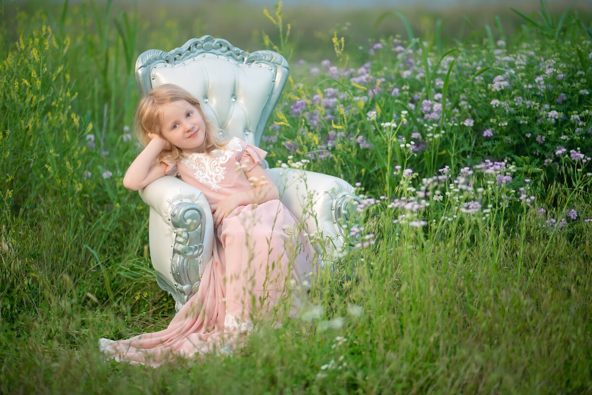 Adorable portrait of a young girl reclining in a meadow, dressed in a flowing pink gown. Captured in Overland Park, Kansas, this whimsical scene is perfect for families seeking natural and serene child photography in the Kansas City area.