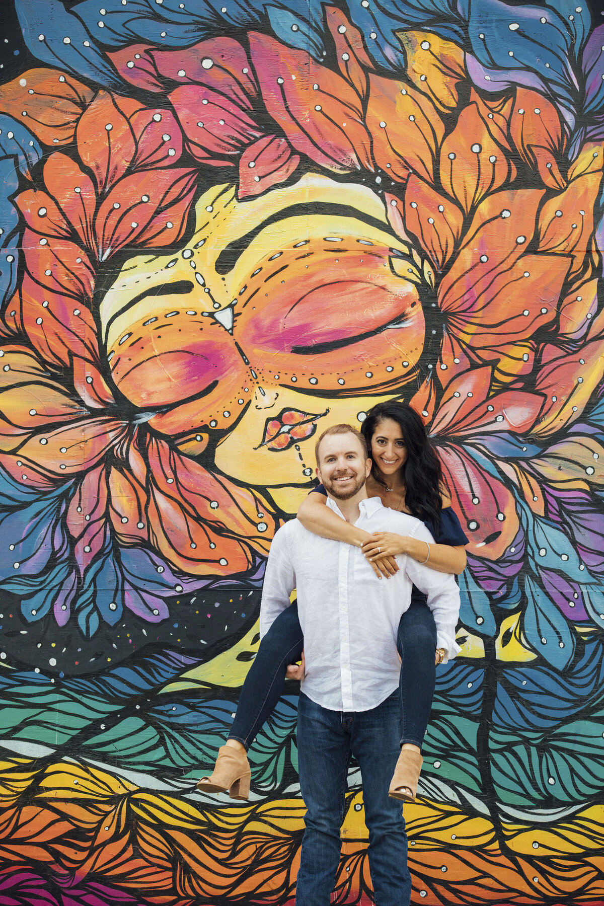 Couple doing piggyback pose by mural wall during engagement photo in Asbury Park New Jersey