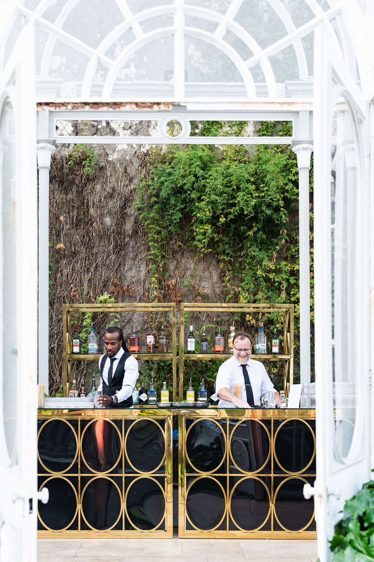 bartenders at a black and gold bar inside avington park’s glasshouse orangery for a luxury 50th birthday party event