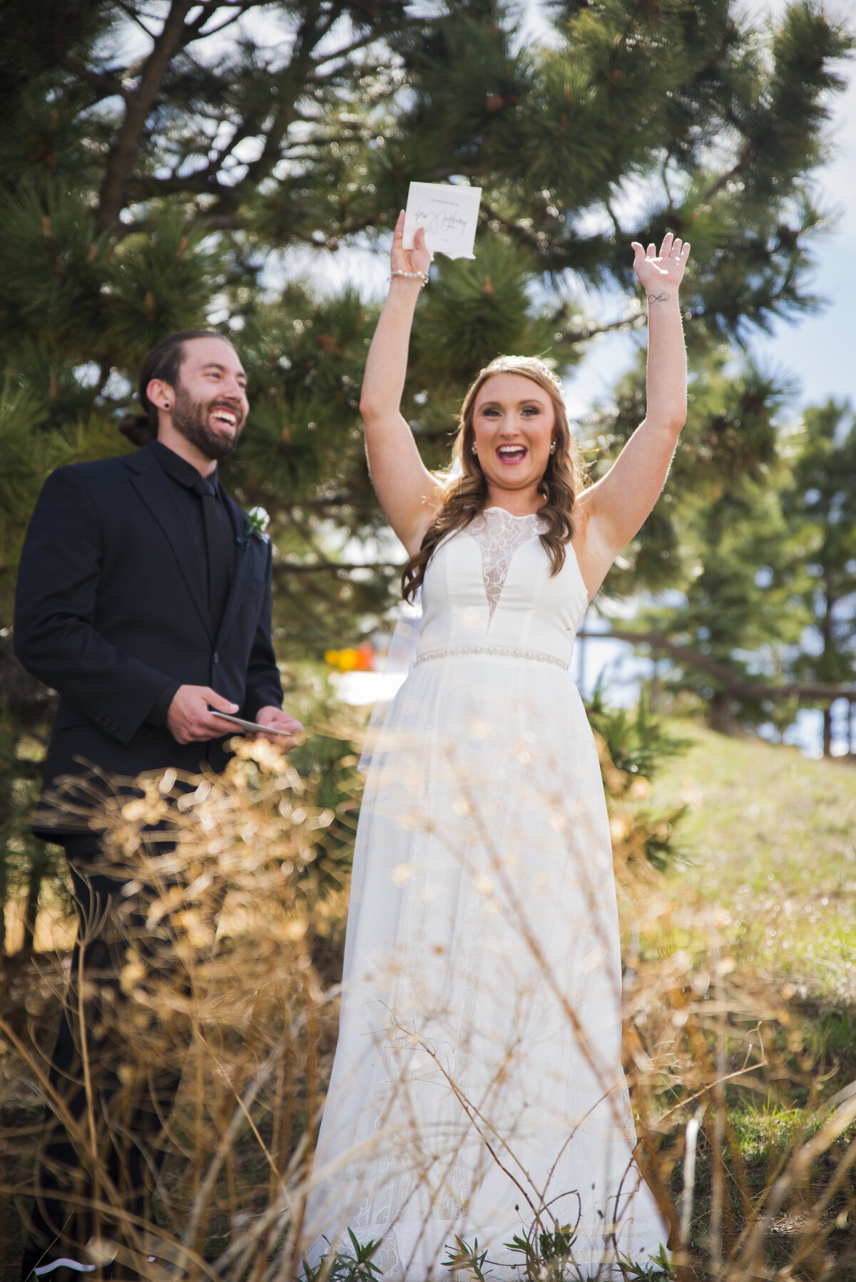 A groom smiles at his bride as she lifts her hands up in celebration.