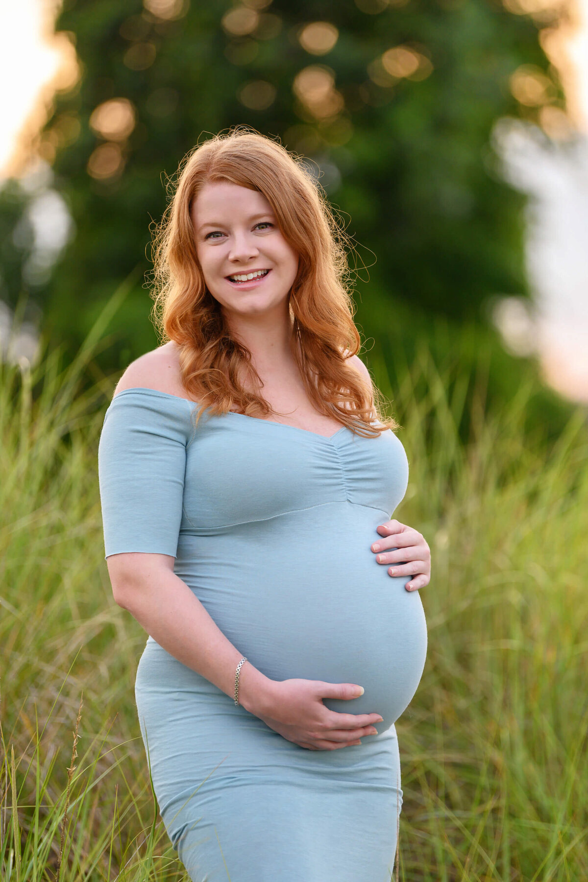 red-haired pregnant woman holding her belly for her outdoor beach maternity photos in Burlington