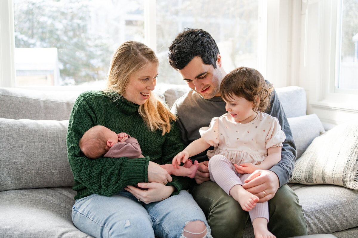Family of four sitting on couch in light filled room